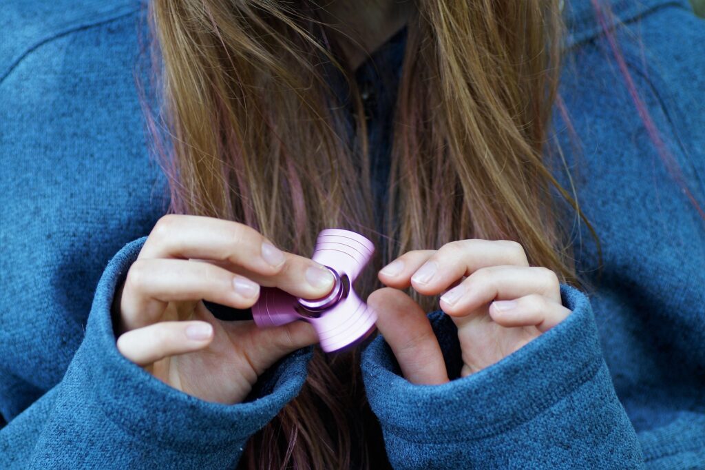 Fidget toy 2026 : jeune fille utilisant un fidget spinner rose en aluminium