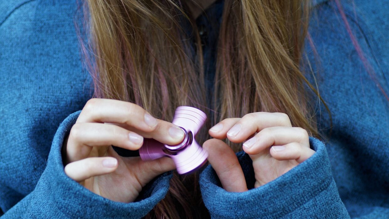 Fidget toy 2026 : jeune fille utilisant un fidget spinner rose en aluminium
